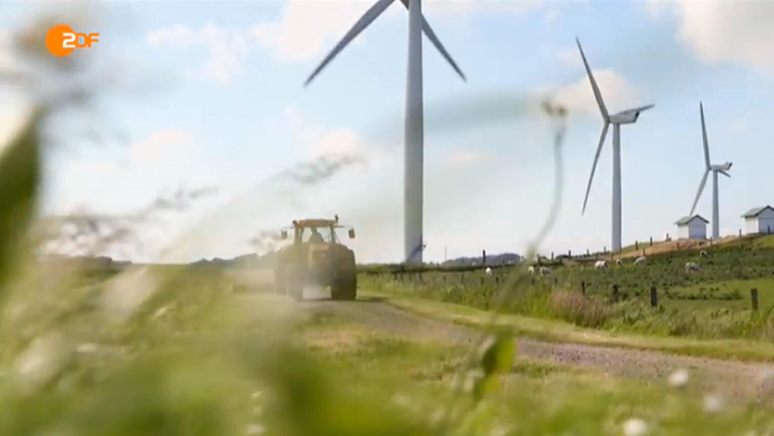 Ausschnitt eines ZDF-Beitrags, auf dem man blauen Himmel über einer Wiese mit Windrädern und einem Trecker sieht.