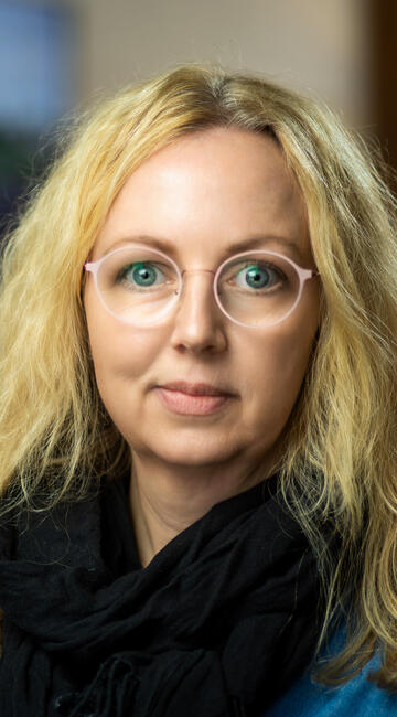 Eine Frau vor einer Wand mit Plänen lächelt in die Kamera.