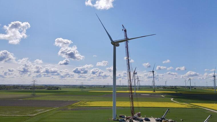 Windräder unter blauem Himmel mit einzelnen Wolken inmitten von grünen und gelben Feldern.