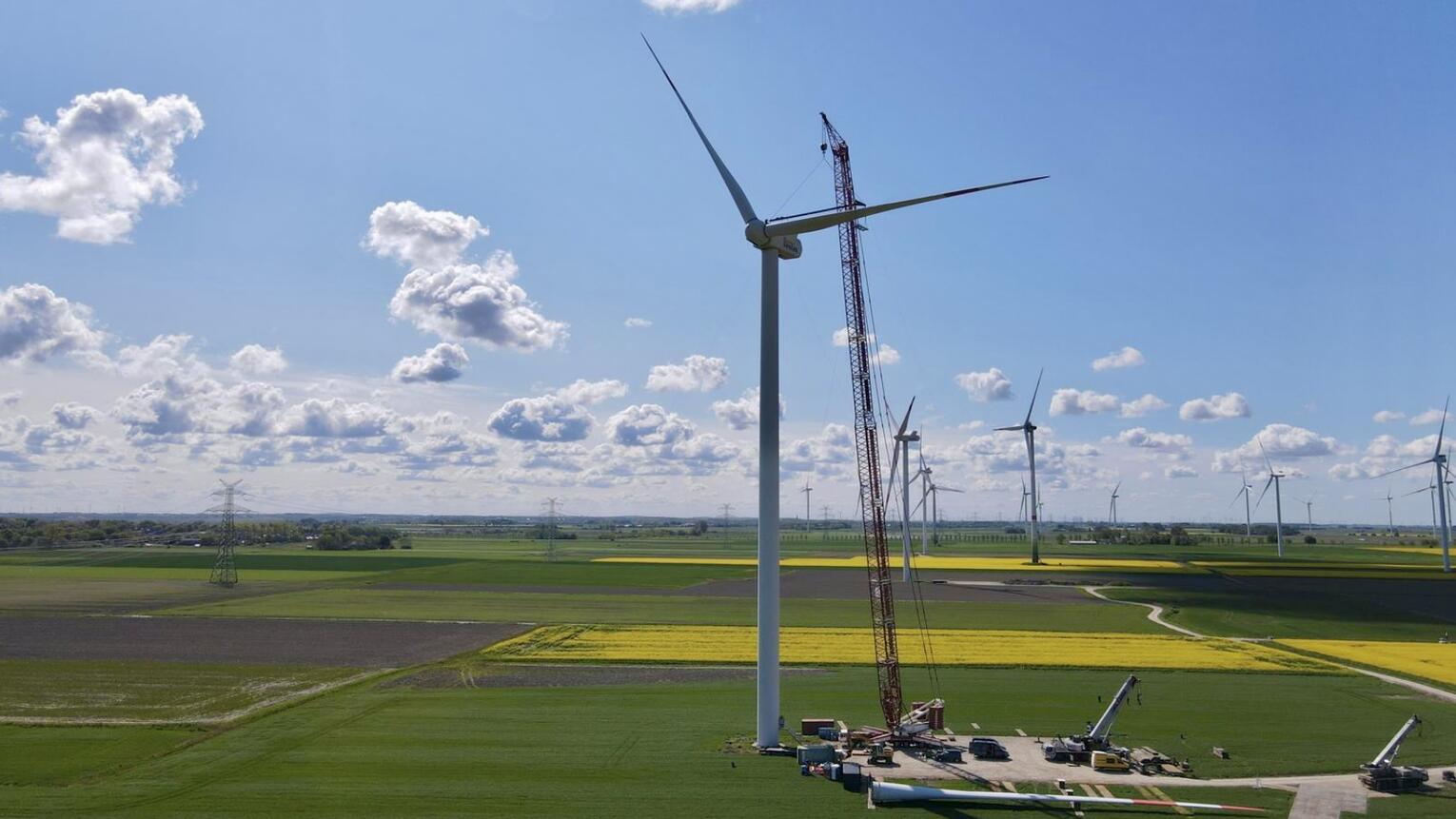 Windräder unter blauem Himmel mit einzelnen Wolken inmitten von grünen und gelben Feldern.