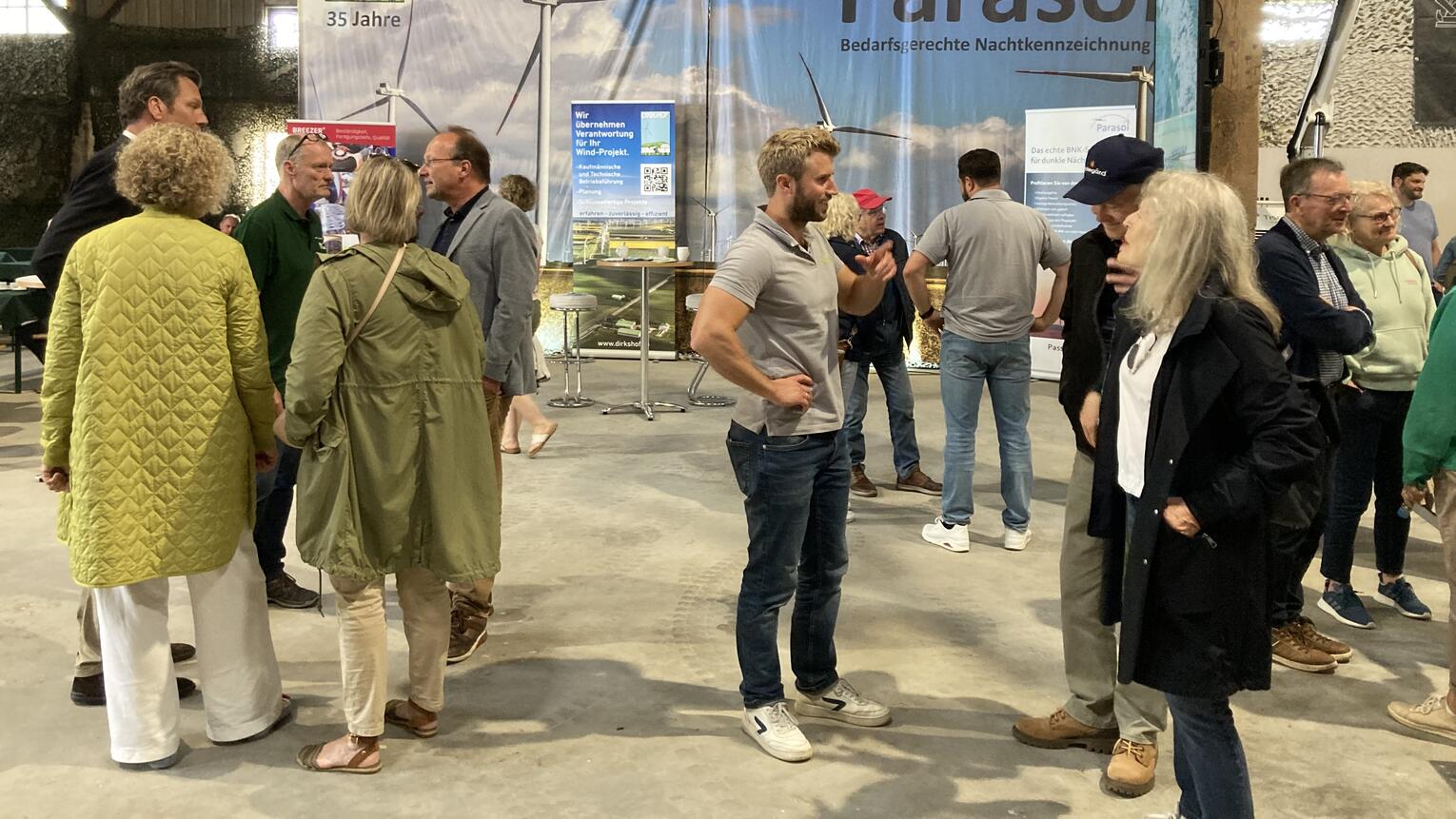 Menschen stehen beim Sönke-Nissen-Koog-Hoftag in Grüppchen verteilt in einer Halle und sprechen miteinander. Im Hintergrund ein großes Plakat mit der Aufschrift PARASOL.