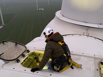 Ein Mann mit Schutzhelm steigt oben durch eine Klappe in eine Windturbine.