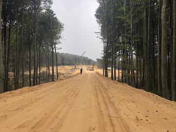 Eine sandige Straße führt zu einer Baustelle mitten im Wald.