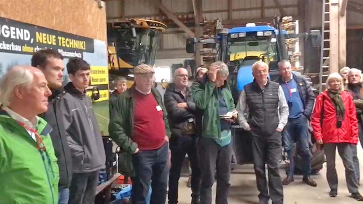 Bei einer Führung durch eine landwirtschaftliche Halle stehen mehrere Personen vor zwei großen Bau- oder Landmaschinen und hören zu.