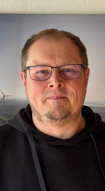 Ein Mann vor einem Bild von einem Windrad lächelt in die Kamera.
