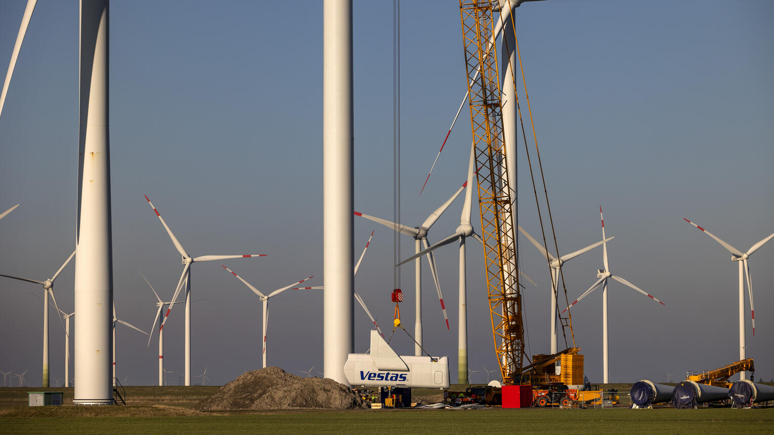 Konstruktion eines Windrads inmitten vieler weiterer Windräder mithilfe eines Krans.