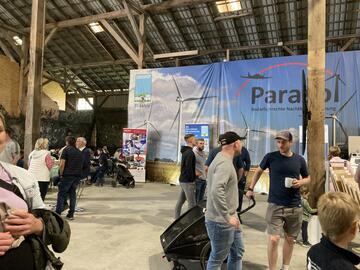 Menschen stehen beim Sönke-Nissen-Koog-Hoftag in Grüppchen verteilt in einer Halle und sprechen miteinander. Im Hintergrund ein großes Plakat mit der Aufschrift PARASOL.