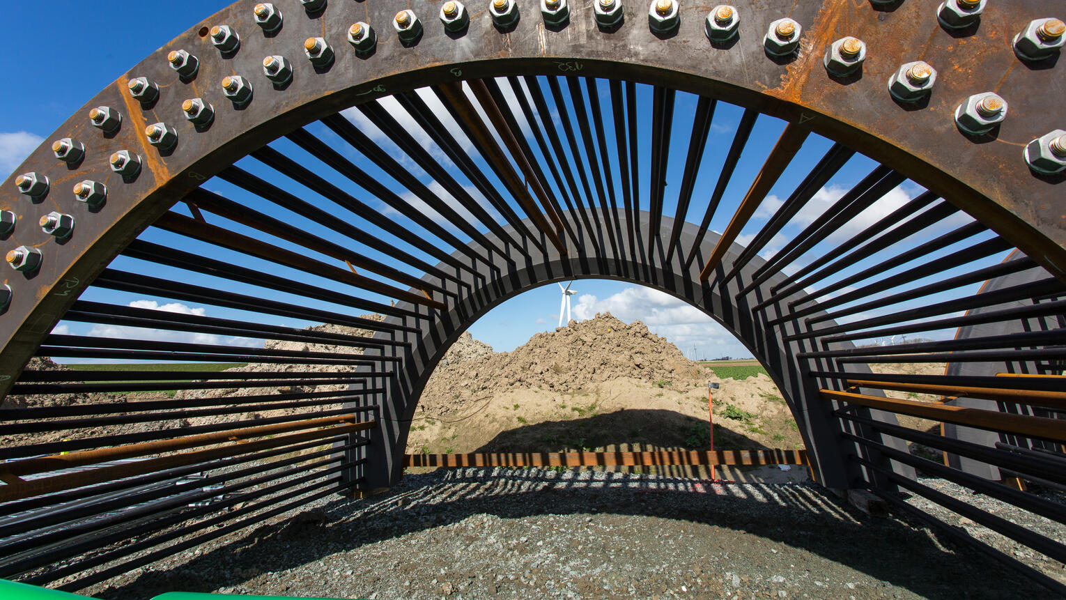 Ein großes Metallteil mit Speichen und Nieten liegt auf der Baustelle eines Windrads bereit.