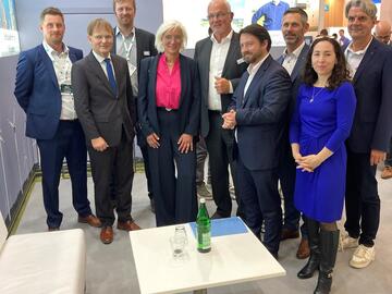 Am Dirkshof-Stand auf der WindEnergy-Messe posieren neun Personen für ein Gruppenfoto.