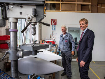 Der Ministerpräsident und ein Mitarbeiter lachend in einer Maschinenhalle.