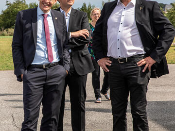 Der Ministerpräsident und Dirk Ketelsen posieren draußen für ein Foto, ein Mann und eine Frau im Hintergrund.