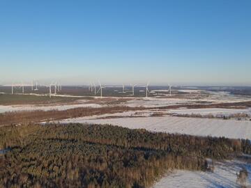 Inmitten von Wald und schneebedeckten Wiesen ragen mehrere Windräder auf.