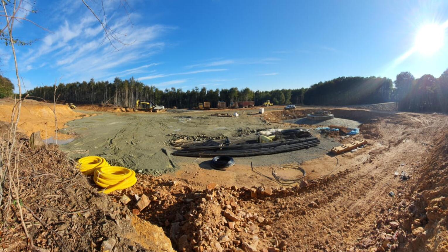 Panorama-Aufnahme einer sandigen Baustelle in einem Wald mit dem Fundament eines Windrads und Arbeitsgeräten ringsum.