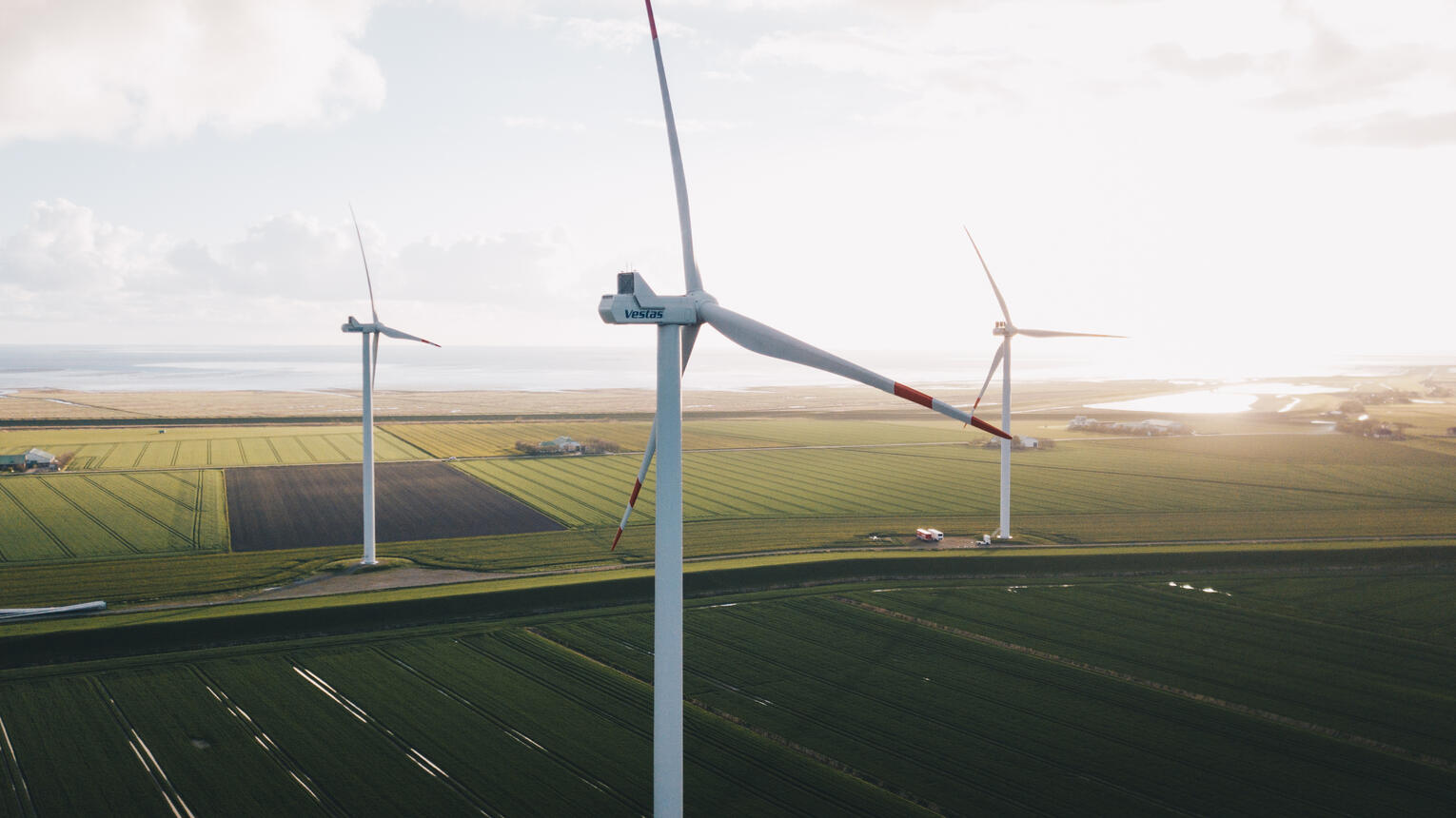 Ein Windpark bei bewölktem Himmel, im Hintergrund Meer.