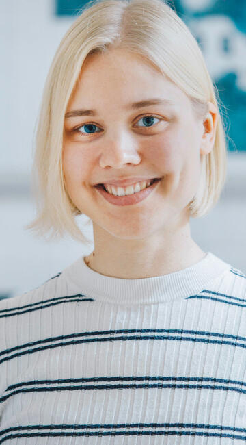 Eine junge Frau in einem hell erleuchteten Raum lächelt in die Kamera.
