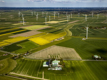 Luftaufnahme des Dirkshofs und des umgebenden Windparks inmitten blühender grüner und gelber Felder.