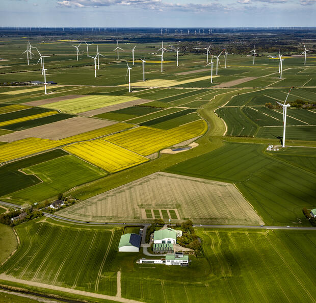Luftaufnahme des Dirkshofs und des umgebenden Windparks inmitten blühender grüner und gelber Felder.