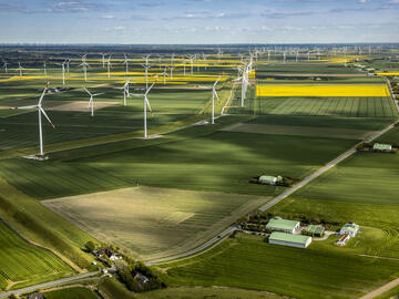 Luftaufnahme des Dirkshofs und des umgebenden Windparks inmitten blühender grüner und gelber Felder.