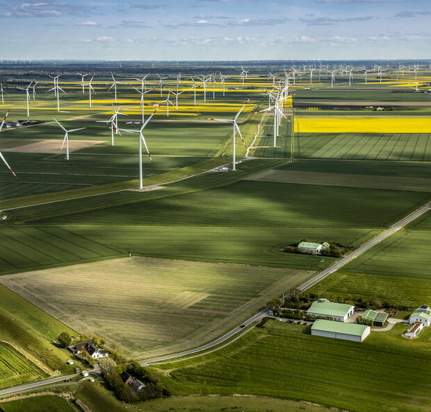 Luftaufnahme des Dirkshofs und des umgebenden Windparks inmitten blühender grüner und gelber Felder.
