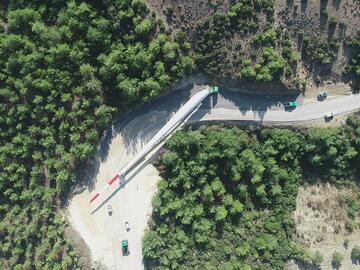 Luftaufnahme eines Rotorblatts eines Windrads, das mit Fahrzeugen durch einen Wald transportiert wird.