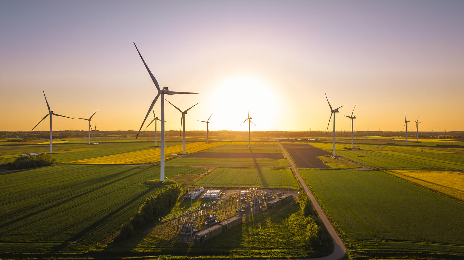 Ein Windpark im Sonnenuntergang, dazwischen grüne Felder.